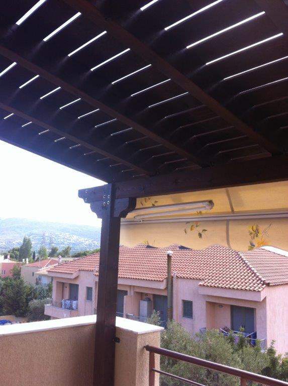 Ξύλινη πέργκολα με δοκούς και σταθερές μόνιμες διακοσμητικές σανίδες στο πάνω μέρος